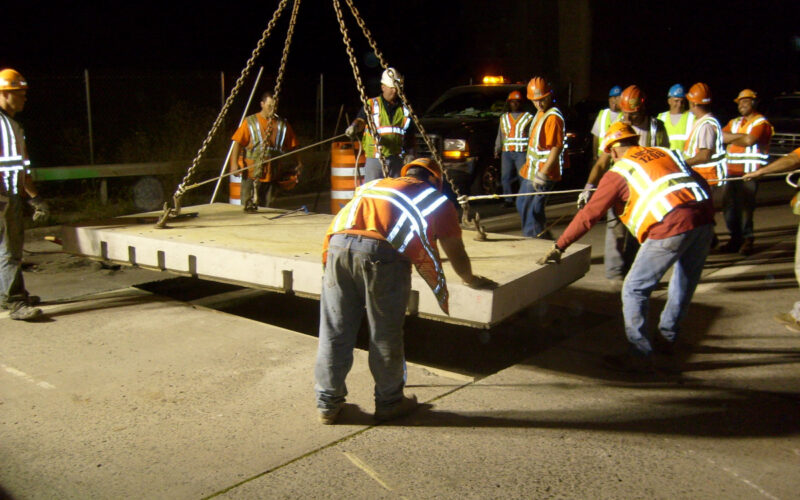 workers moving pavement block with crane system